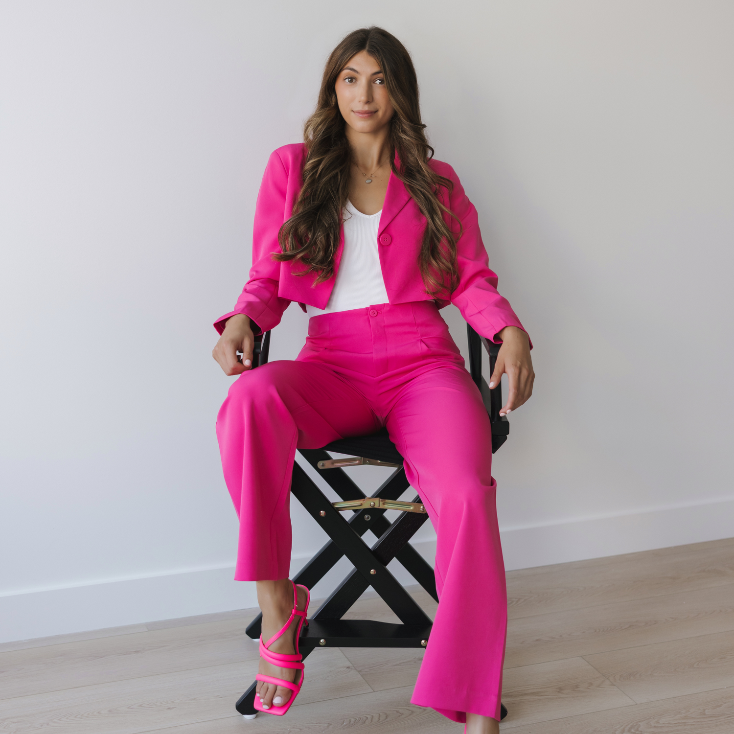 Woman in a bright pink suit sitting on a director's chair against a white wall.